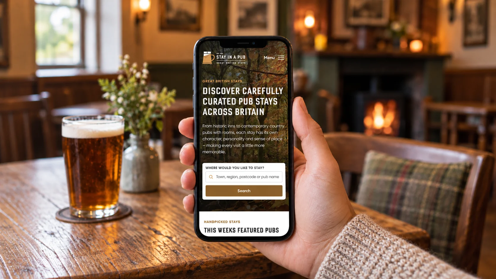 A visitor holding a phone showing the Stay in a Pub homepage in a cosy pub.